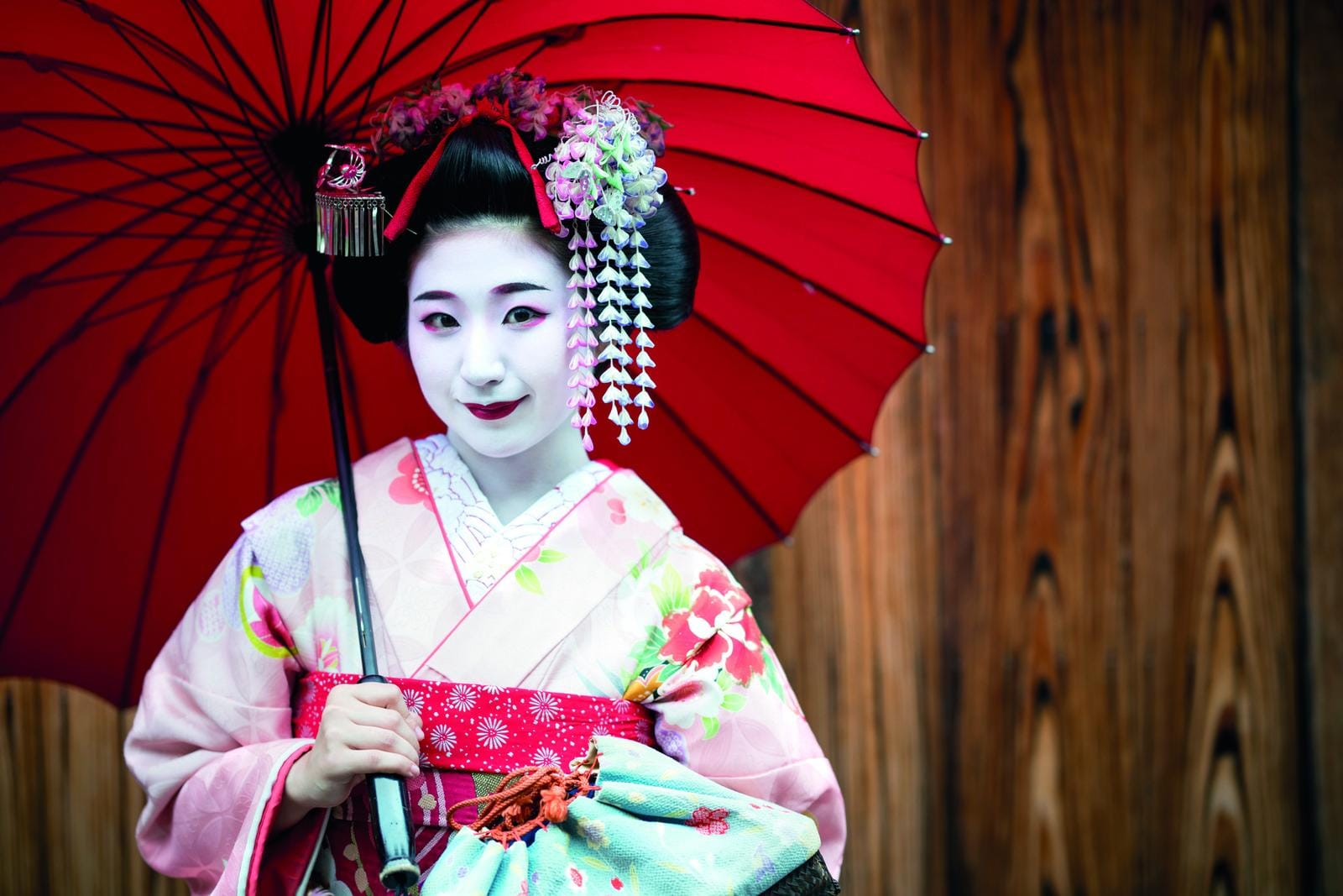 Kimonotragende Frau mit rotem Schirm vor Holzwand in Japan.