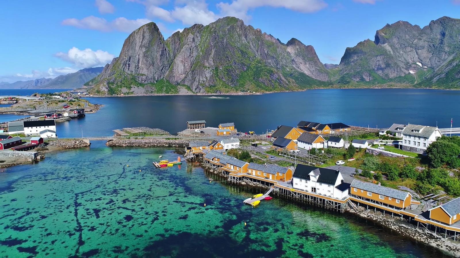Norwegen, Lofoten-Inseln, malerische Küstenhäuser am klaren blauen Wasser mit Bergkulisse.
