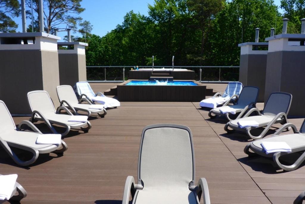 Sonnenterrasse mit Pool und Liegestühlen, umgeben von Bäumen, ideal für Erholung.