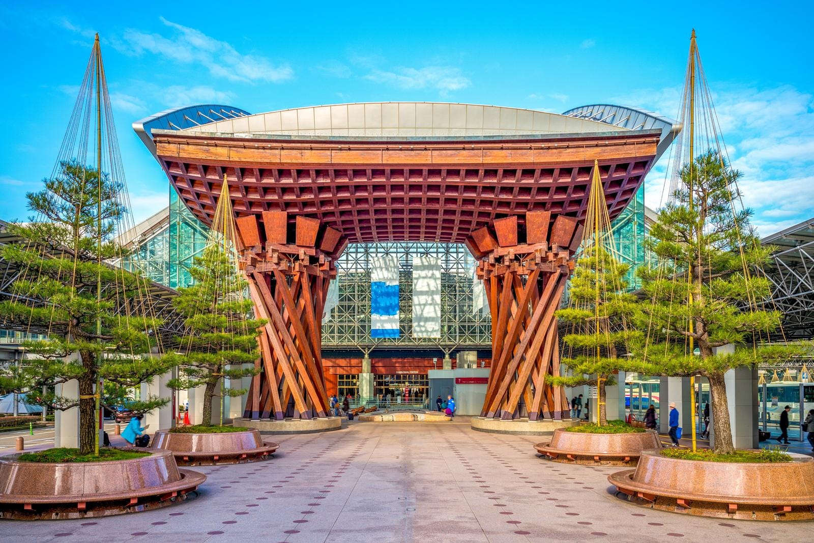 Holztor am Bahnhof Kanazawa, Japan, umgeben von Bäumen und blühendem Himmel.