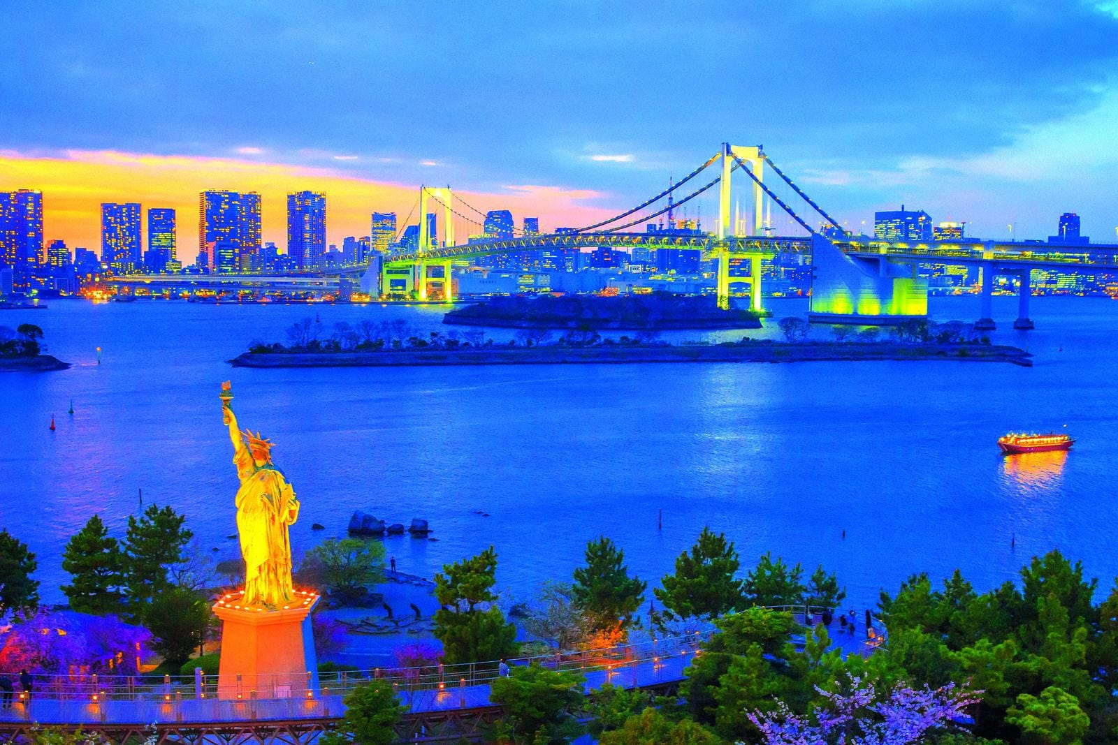 Abendblick auf Tokios RegenbogenbrĂĽcke und Freiheitsstatue vor beleuchteter Skyline.
