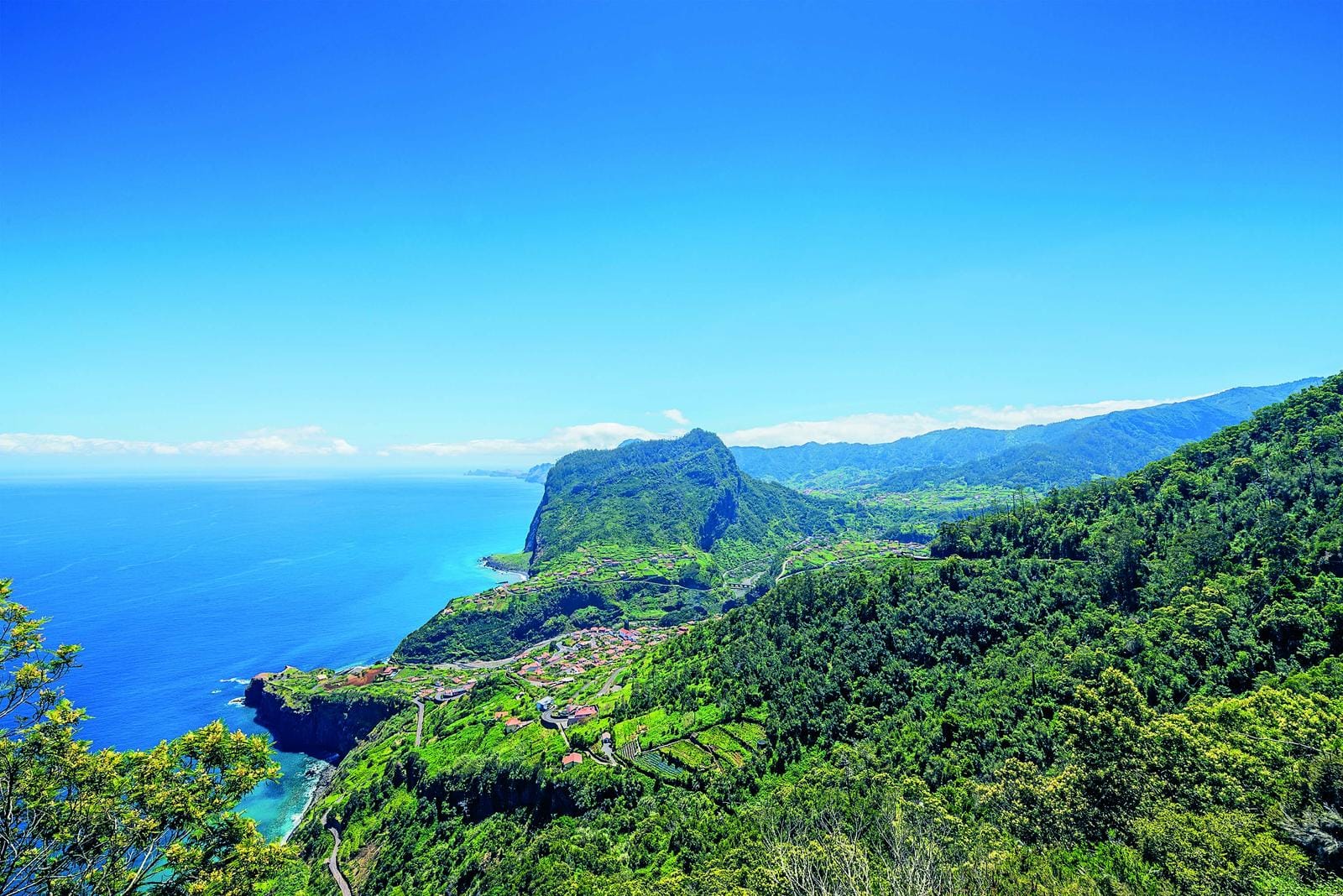 Grüne Berge und Küstenpanorama auf Madeira, Portugal, unter strahlend blauem Himmel.