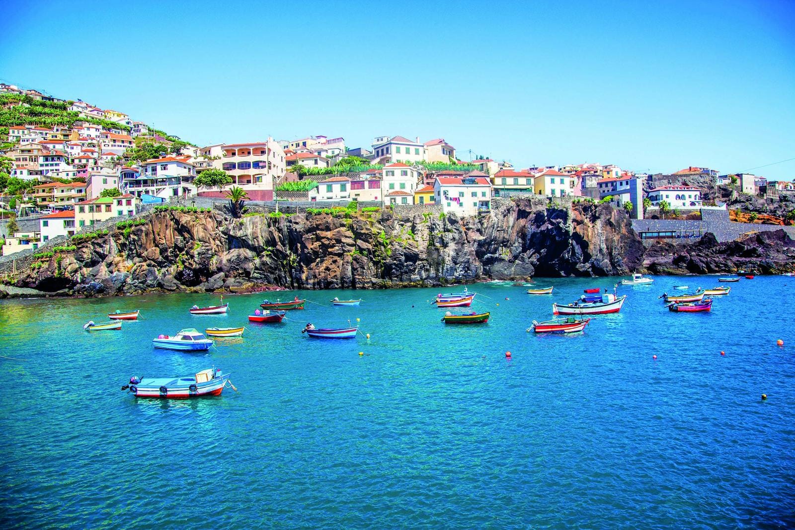 Bunte Boote schaukeln in der Bucht von Madeira, Portugal, umgeben von malerischen Häusern.