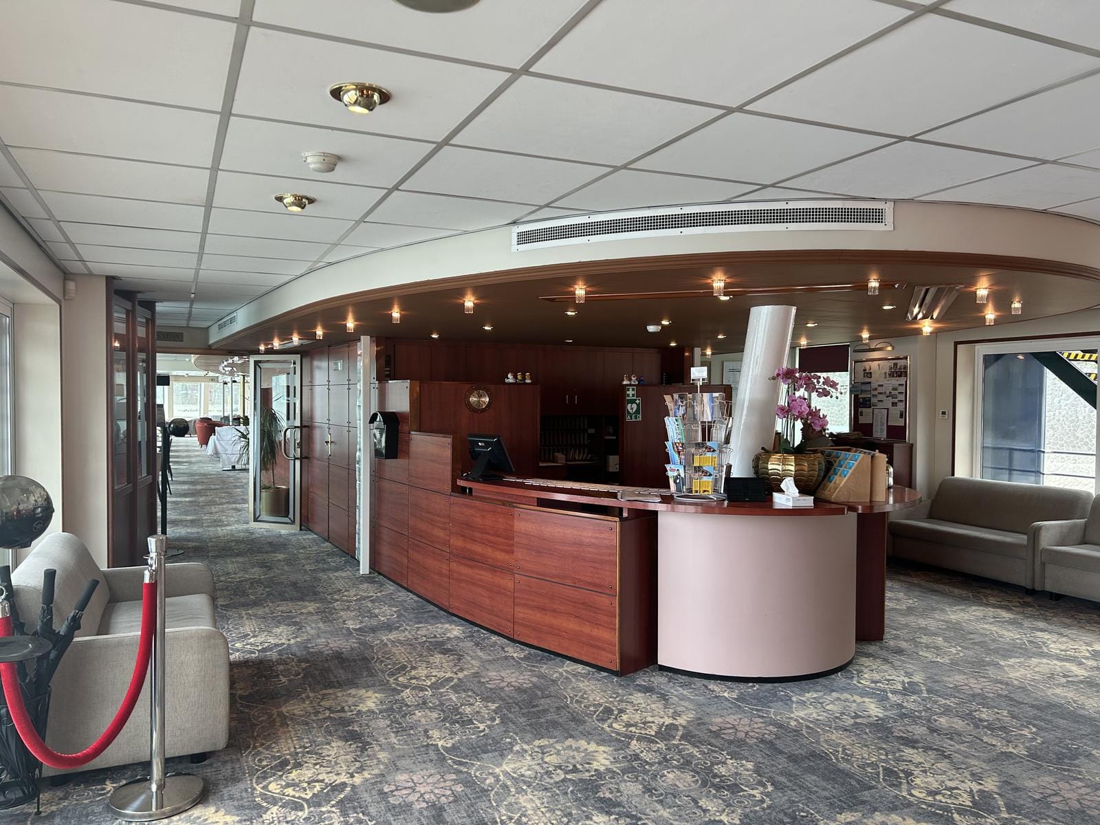 Empfangsbereich eines Hotels oder Schiffs, stilvoll mit Holz und Blumendeko gestaltet. Ort unbekannt.