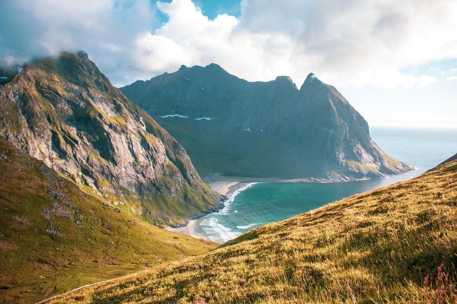 Norwegen, Lofoten: Dramatische Berge, grünes Tal, strahlend blauer Ozean unter Wolken.