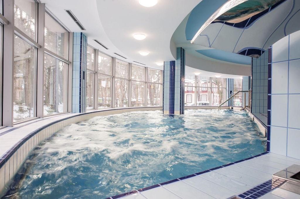 Modernes Hallenbad mit Whirlpools in einem Resort, umgeben von winterlichem Wald in Lettland.