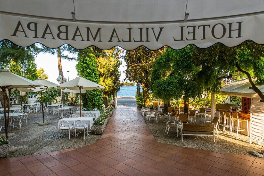 Gemütliche Hotelterrasse mit weißen Tischen, grüner Bepflanzung und Blick auf das Meer.