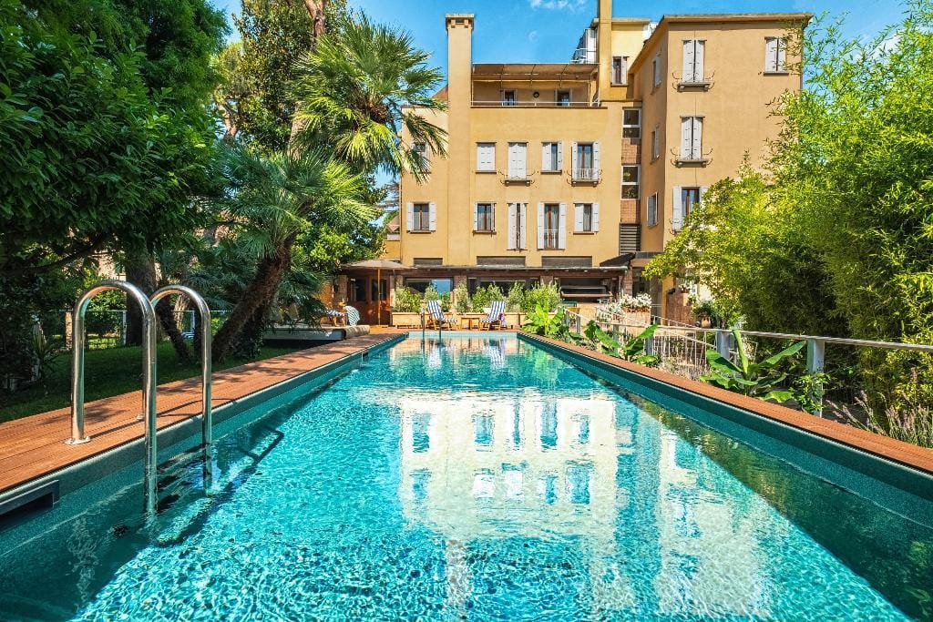 Langer Pool neben Palmen und grünem Gebäude mit geschlossenen Fensterläden.