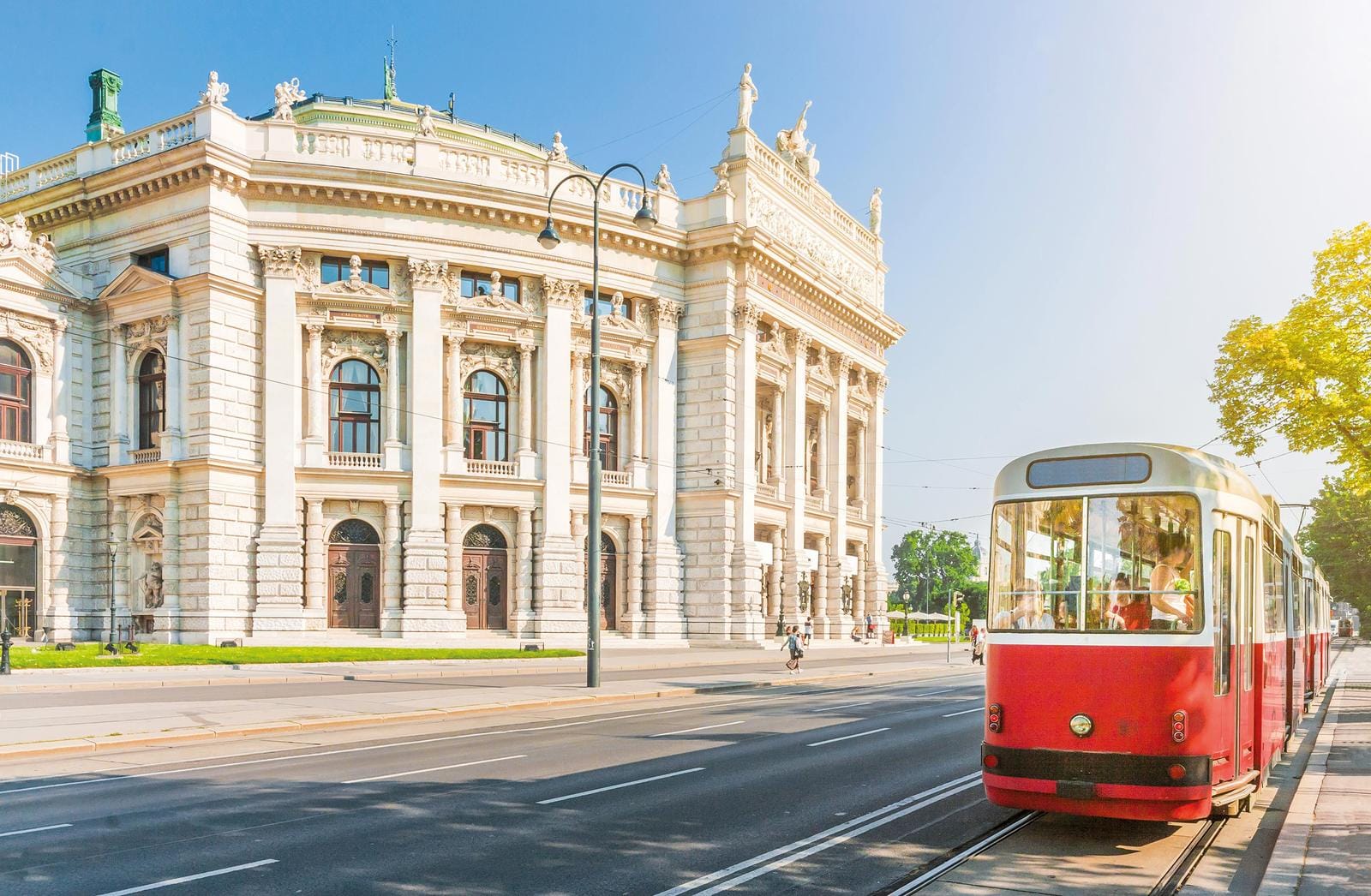 Historisches Gebäude und rote Straßenbahn in Wien bei sonnigem Wetter.