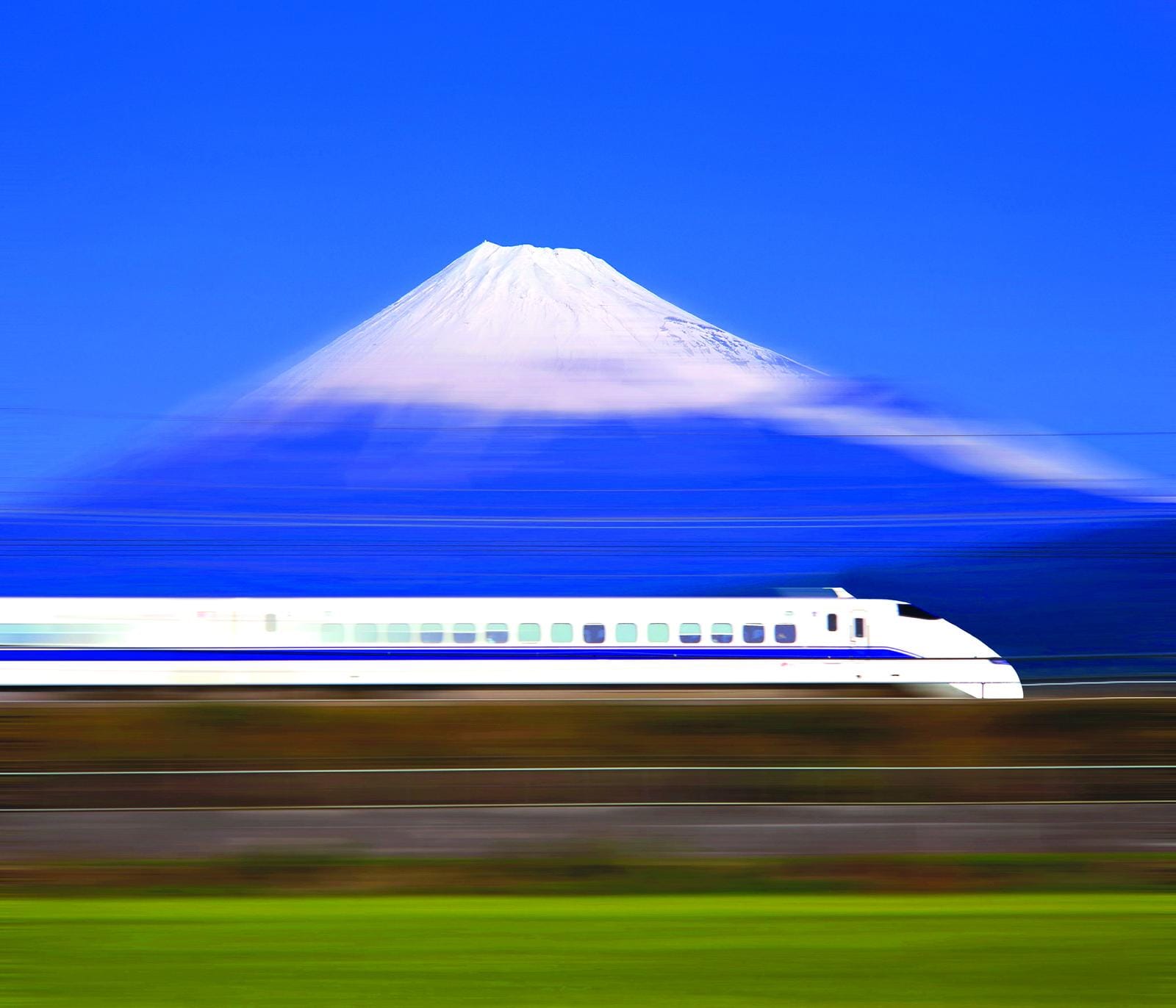 Japan, Mount Fuji und vorbeifahrender Shinkansen-Zug bei klarem, blauen Himmel.